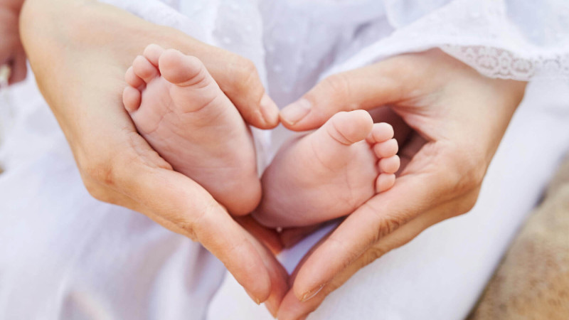 Hände umschließen zarte Füße eines Babys, Symbol für Kinderherzerkrankungen.